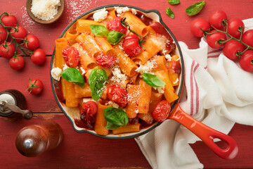 Pasta Tortiglioni with tomato sauce, baked cherry tomatoes, mozzarella and parmesan cheese, basil on old red rustic table. Traditional Italian cuisine. Example Italian food for article. Top view.