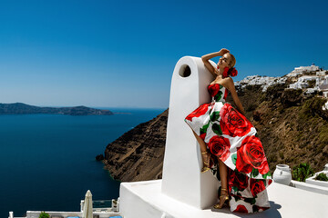 Beautiful elegant woman in long floral gown dress is posing in luxury resort in Santorini. Female...