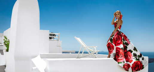 Beautiful elegant woman in long floral gown dress is posing in luxury resort in Santorini. Female...