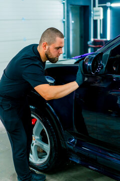Focused Male car wash worker in black gloves polishes the mirror of a luxury blue car using a polishing sponge car care concept 