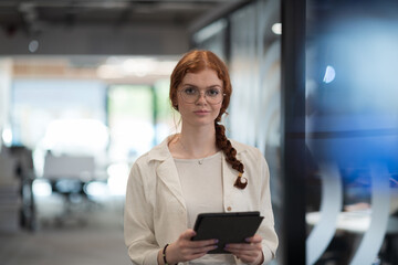 A young business woman with orange hair self-confident, fully engaged in working on a tablet, exuding creativity, ambition and a lively sense of individuality