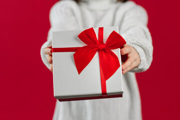 Close up of girls hands holding white red gift box, offering and giving Christmas gifts, red background. Christmas, New Year, winter holiday concept