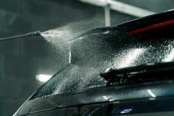 Close-up of the rear window of a black car at the moment of applying car wash from a spray bottle in a car wash box