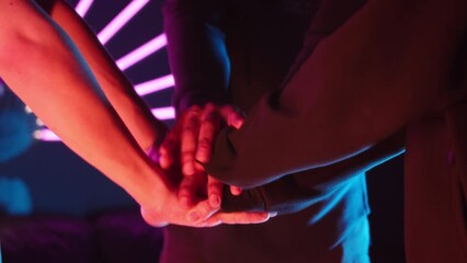 Cropped slowmo shot of unrecognizable team of professional gamers putting their hands together while getting ready for important gaming championship in dark cybersport club