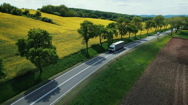 Aerial view truck and trailer driving on a scenic country highway along a flowering yellow field. Trucking, cargo delivery, transportation, import, export. 4k footage