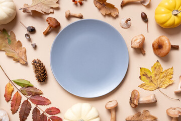 Empty plate with pumkins, mushrooms and autumn leaves on beige background top view. Monochrome autumn flat lay