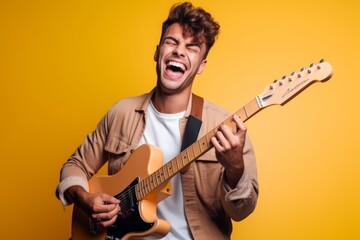 Portrait of a happy young man playing guitar isolated over yellow background