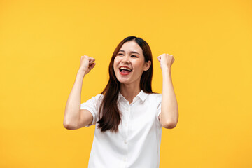 Young asian woman wearing white short sleeve shirt and raising arms while smiling and screaming to...