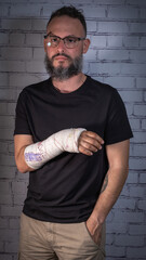 Young bearded man with glasses, wearing a black T-shirt. Broken arm with plaster painted with children's drawings. Tenerife, Canary Islands, Spain.
