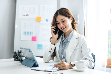 Businesswoman is reading marketing plan report and talking on smartphone while working to analysis