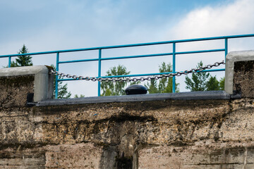 Fototapeta premium A fragment of the wall of an old lock with a mooring bollard and a chain.