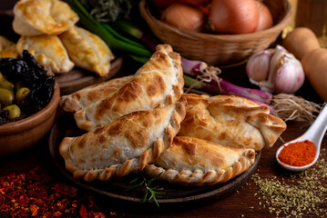 homemade meat chicken and ham and cheese empanadas on wooden board and vegetables around and...