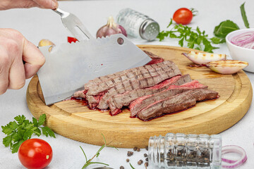 Woman cuts grilled steak. Female hands with knife and two pronged fork. Fresh herbs, vegetables