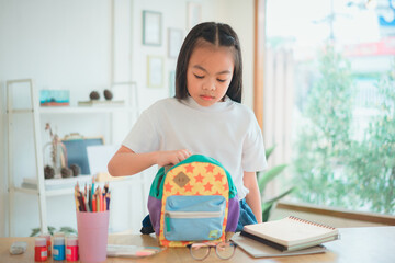 Fototapeta na wymiar Pupil child put books and notes into backpack. School supplies.Back to school concept. Kid prepare for studies. Portrait cute little girl packing backpack .