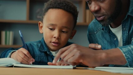 African American cute little boy child schoolboy with ethnic adult father writing homework. Dad help son with lesson class write explain exercise task kid close ears homeschooling elementary education - Powered by Adobe