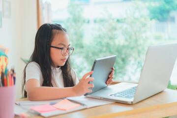 Fototapeta premium Asian school girl doing homework at laptop raising hand pointing finger . The girl does his homework. Home schooling.