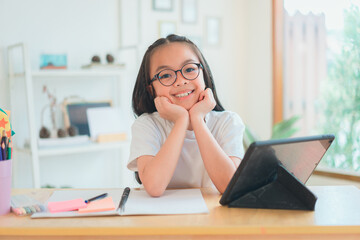 Asian school girl doing homework at laptop raising hand pointing finger . The girl does his homework. Home schooling.