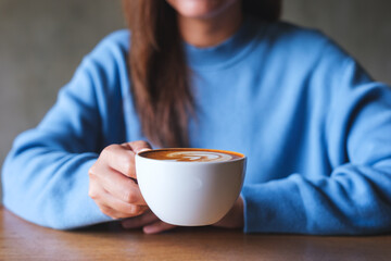 Closeup image of a woman holding a cup of latte coffee