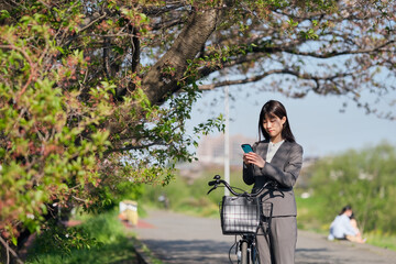 Fototapeta na wymiar 木の下で自転車を降りてスマートフォンを見る女性