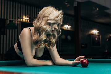 Blond woman playing enjoying billiard, balls on table with green surface in billiard club. Pool game snooker pyramid player

