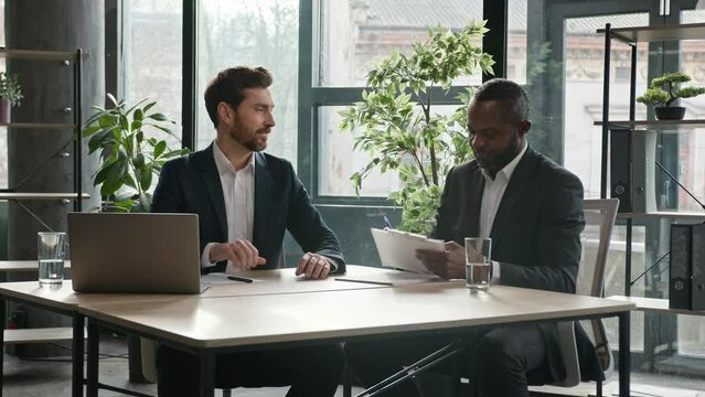 Moving camera diverse businessmen in office sign contract handshake cooperation Multiethnic Caucasian and African American business people men at desk signing document shake hands success partnership