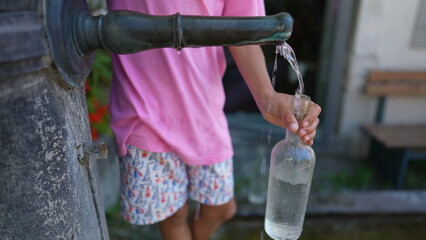 Kid filling bottle glass water from public faucet