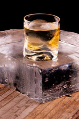 single malt whiskey on the rocks with clear ice in sphere isolated on wooden table over angled block of ice