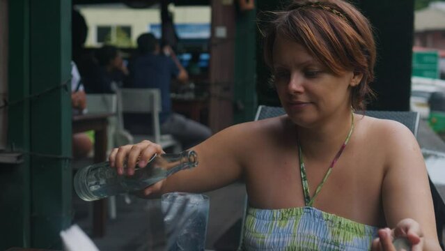 Beautiful girl in street cafe pours water from bottle into glass and drinks.