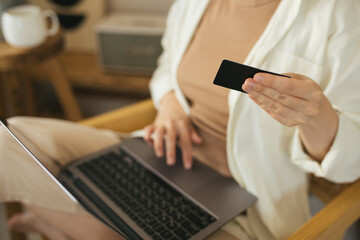 Young woman shopping online, using laptop and credit card, sitting in a cozy living room.