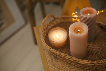 Burning candles on wicker tray in a cozy room with lights on the background.