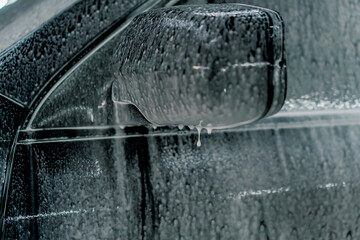 Close-up of car foam on the mirror of a black luxury car in a car wash box 