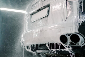Close-up of car foam application on the trunk, rear bumper and exhaust pipe of a black luxury car in the car wash box 