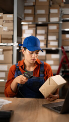 Female worker in warehouse using bar code scanner to scanning box sitting at the table. Working at...