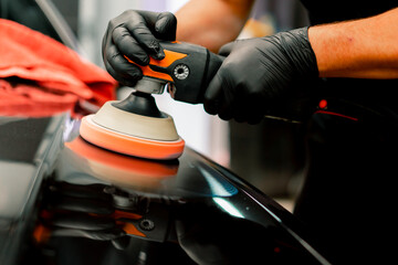 Close-up of a car wash worker using a polishing machine to polish the hood of a black luxury car  - obrazy, fototapety, plakaty