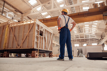 Male builder in work overalls observing building under construction