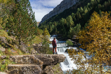 waterfall with male hiker in Ordesa valley during autumn in the pyrenees mountains, Ordesa and Monte Perdido National Park, Huesca, Aragon, Spain