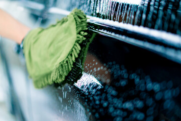 Close-up of a car wash worker using a green washcloth to wash a black luxury car with car wash...
