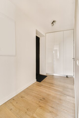 an empty room with white walls and wood flooring on the right, there is a black door to the left