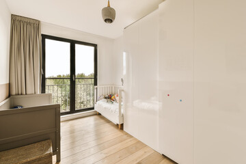 a bedroom with wood flooring and white cupboards on the wall, there is a window to the outside