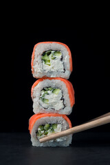 Sushi Rolls on a black background. Chopsticks take a roll. Traditional Japanese Cuisine