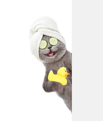 Happy cat with  pieces of cucumber on it eyes  and with towel on it head holds rubber duck behind empty white banner. isolated on white background