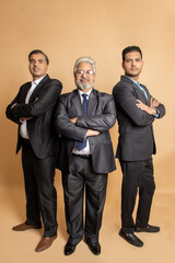 Group of positive indian businessmen wearing suit standing cross arms looking at camera with smiles isolated on beige studio background. corporate people.