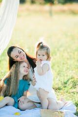 Beautiful young mother with little daughters on a picnic in the field. Summer breakfast with lemons. Family.