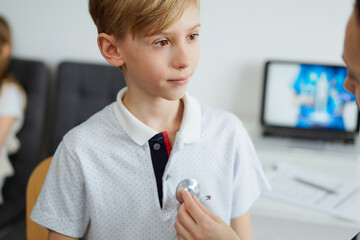 Doctor and kid patient are in the clinic. Physician in white coat examining a serious young boy with a stethoscope, close up. Medicine, therapy concept