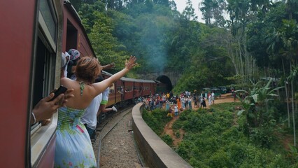 Nine Arches Bridge. Girl leans out of moving train waves to crowd on platform.