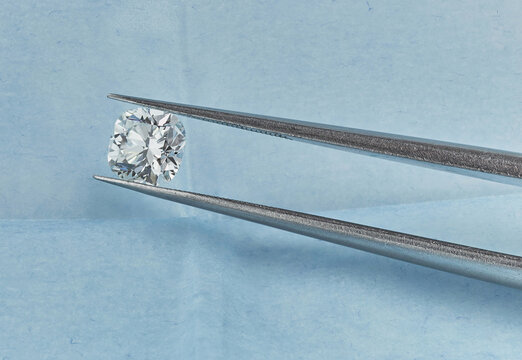 Cushion Cut Diamond. Macro Diamond Photograph of Fancy Cushion Diamond in Blue Parcel Background with Tweezers. 
