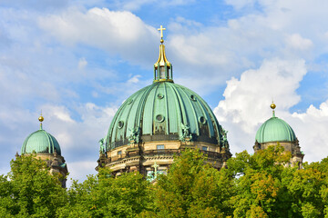 Three green domes of an old Protestant church against a background of blue sky and trees. Religious architecture. Germany, Berlin Cathedral, August 2022.