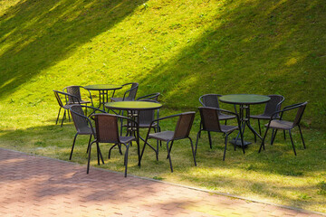 Fototapeta premium Brown chairs and round tables set in the garden at a cafe, outdoor zone, outside seating.