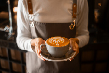Latte art in barista hand ready to drink in modern coffee shop