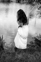 Portrait on back view of  woman wearing a white dress standing in the water of a lake in black and white - 625987382